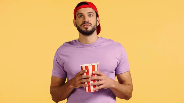 Man watching movie and holding popcorn bucket isolated on yellow — стоковое фото