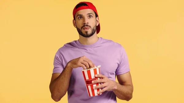 Man watching movie and reaching popcorn bucket isolated on yellow — Stock Photo