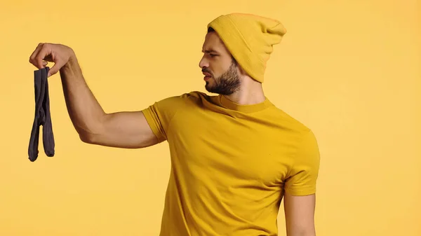 Dissatisfied man looking at stinky socks isolated on yellow — Stock Photo