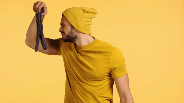 Hombre asqueado oliendo calcetines apestosos aislados en amarillo — Stock Photo