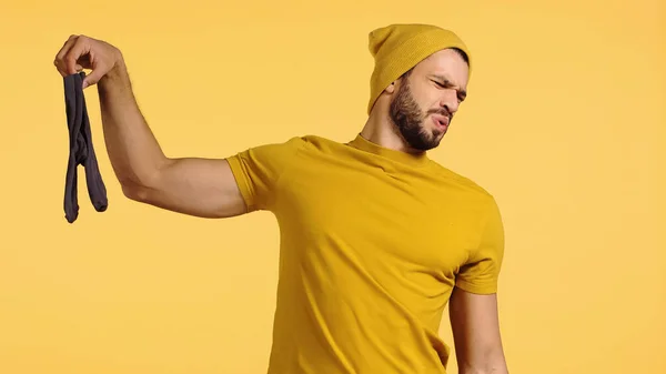 Hombre insatisfecho sosteniendo calcetines apestosos aislados en amarillo - foto de stock