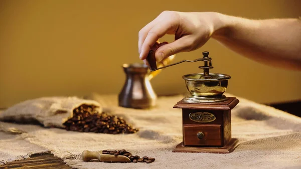 Abgeschnittene Ansicht eines Mannes, der Kaffeebohnen in der Nähe einer verschwommenen Kaffeekanne mahlt — Stockfoto