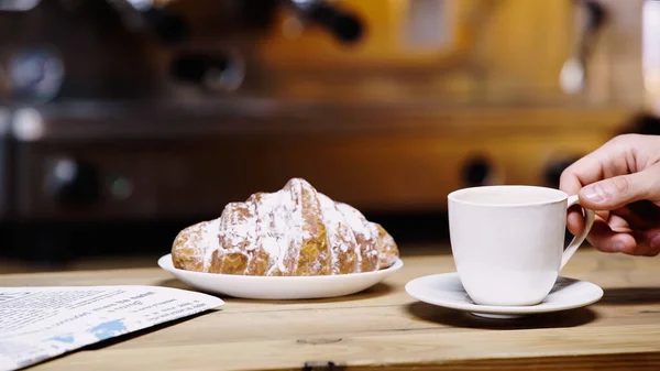 Cropped view of man taking cup near croissant in coffee shop — Stock Photo