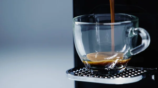 Close up of automatic coffee maker pouring hot beverage into cup on grey — Stock Photo