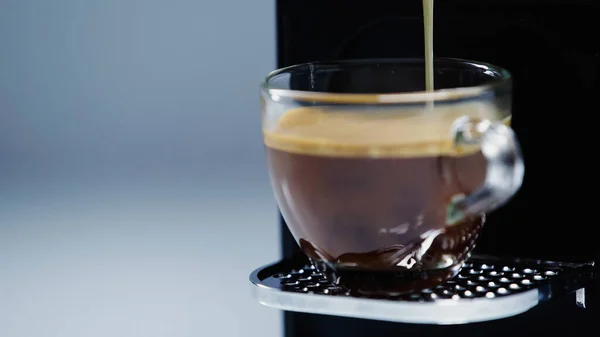 Nahaufnahme einer automatischen Kaffeemaschine, die Getränke in Glasbecher auf grau gießt — Stockfoto
