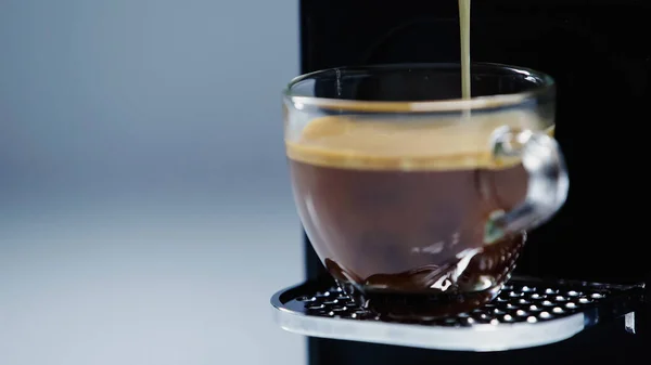 Close up of automatic coffee maker pouring beverage into glass cup on grey — Stock Photo