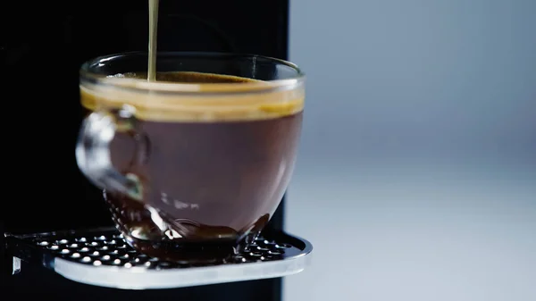 Primo piano di caffettiera automatica versando bevanda in tazza su grigio — Foto stock