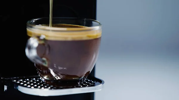 Close up of automatic coffee maker pouring drink into cup on grey — Stock Photo