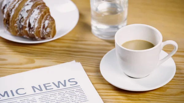 Cup of coffee with milk near newspaper, glass of water and croissant — Stock Photo