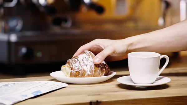 Cropped view of man taking croissant near cup in coffee shop — Stock Photo