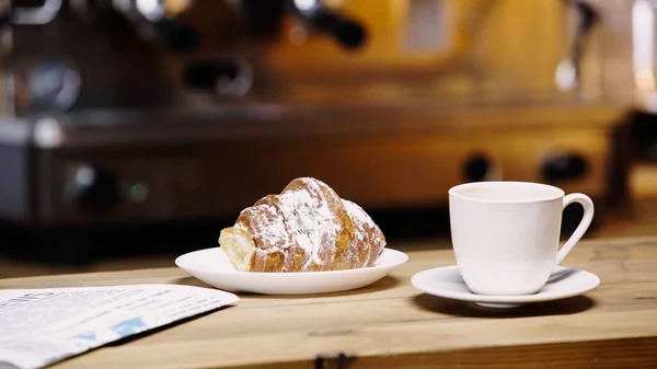 Tasse Kaffee neben leckerem Croissant und Zeitung auf dem Tisch — Stockfoto
