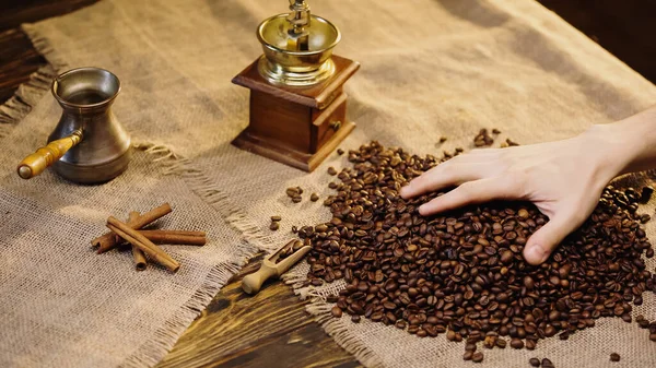 Cinnamon sticks near man taking fresh coffee beans on canvas — Stock Photo