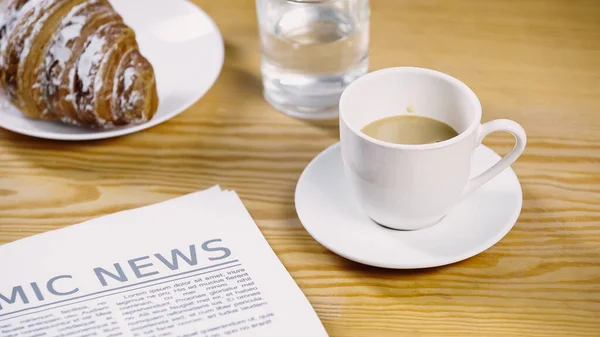 Coffee with milk in cup near newspaper and croissant — Foto stock