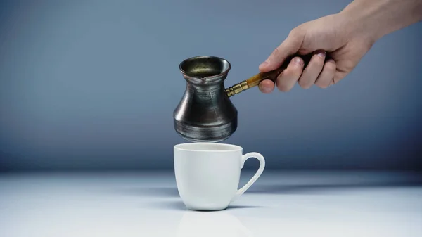 Vue recadrée de l'homme tenant cezve près de tasse sur blanc et gris — Photo de stock