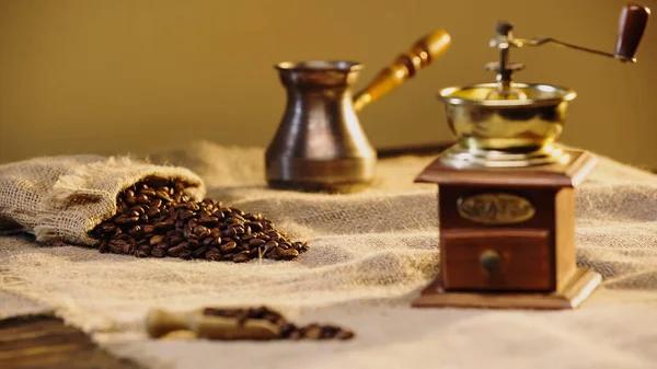 Kaffeebohnen in Leinentasche in der Nähe einer verschwommenen Kaffeemühle — Stockfoto