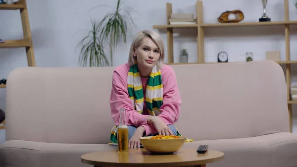 Sad woman sitting on sofa near chips and beer while watching sport match on tv — Fotografia de Stock