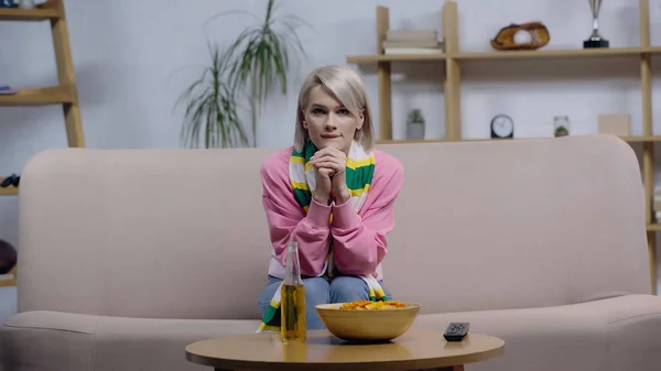 Preocupado fã mulher esporte no cachecol listrado assistindo jogo na tv perto de cerveja e batatas fritas — Fotografia de Stock