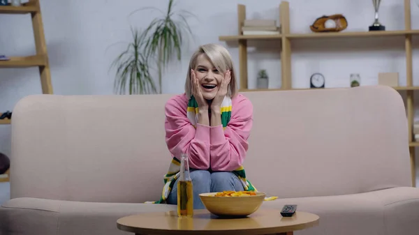 Excité fan de sport femme rire et toucher le visage tout en regardant match près de frites et de bière — Photo de stock