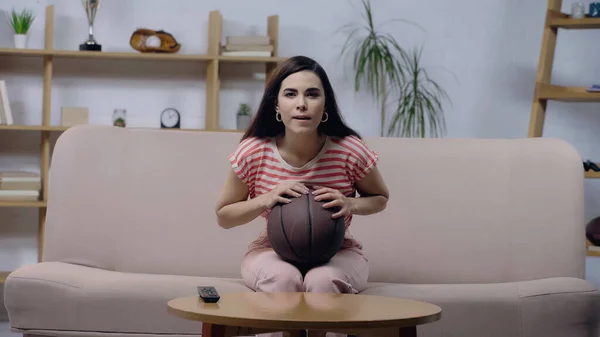 Jovem mulher concentrada assistindo jogo de basquete no sofá em casa — Fotografia de Stock