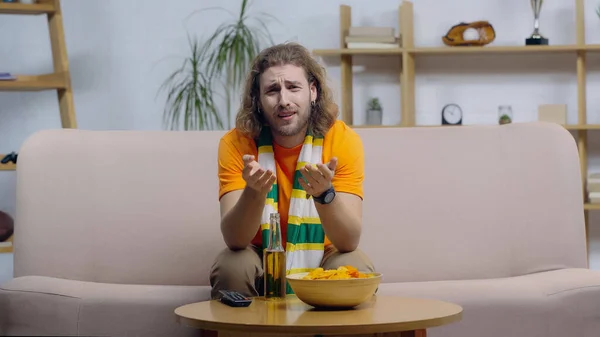 Displeased sport fan frowning and pointing with hands while watching match on tv at home — Fotografia de Stock