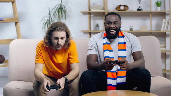 KYIV, UKRAINE - DECEMBER 22, 2021: laughing african american man playing video game near frustrated friend — Foto stock