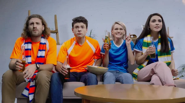 Amusements sportifs excités et inquiets avec des bouteilles de bière regarder le championnat sur le canapé à la maison — Photo de stock