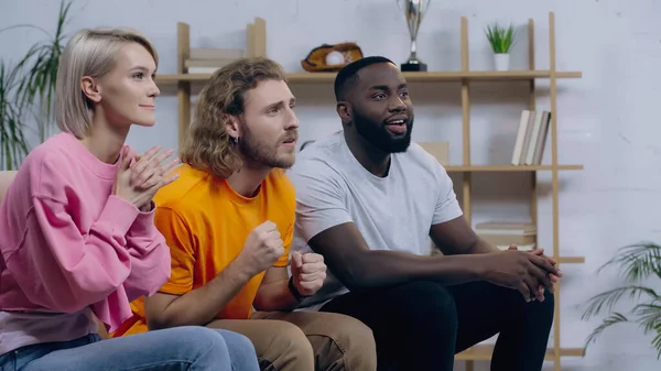 Worried man holding clenched fists for luck while watching match with multiethnic sport fans — Stockfoto