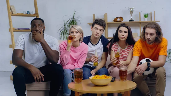 Young woman drinking beer while watching football championship with multiethnic friends — Stock Photo