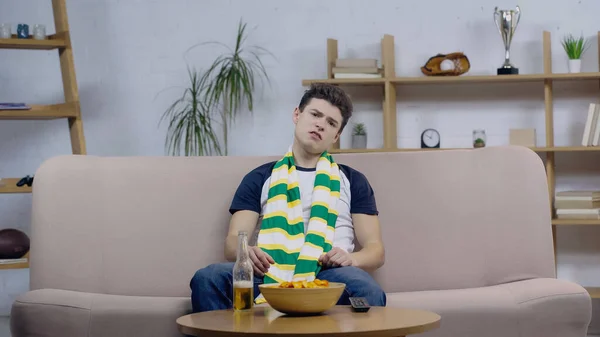 Розчарований фанат спорту сидить на дивані біля пива і чіпсів під час перегляду гри по телевізору — стокове фото