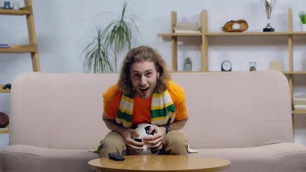 Astonished sport fan with soccer ball shouting while watching football championship on home tv — Stock Photo