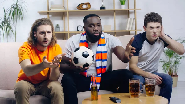 Displeased multiethnic sport fans pointing with hands while watching football match at home — Fotografia de Stock