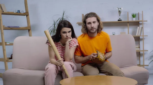 Chateado amigos com equipamentos de softball sentado no sofá e em casa e assistir jogo na tv — Fotografia de Stock