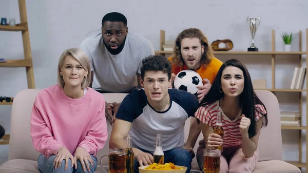 Amigos multiculturales tensos viendo el partido de fútbol en casa tv - foto de stock