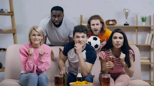 Worried women watching football match with multiethnic friends and holding clenched fists for luck — Fotografia de Stock