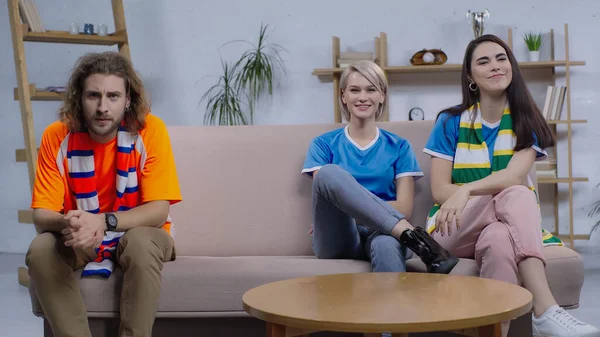 Cheerful women watching sport match while sitting on sofa near frustrated man — Fotografia de Stock