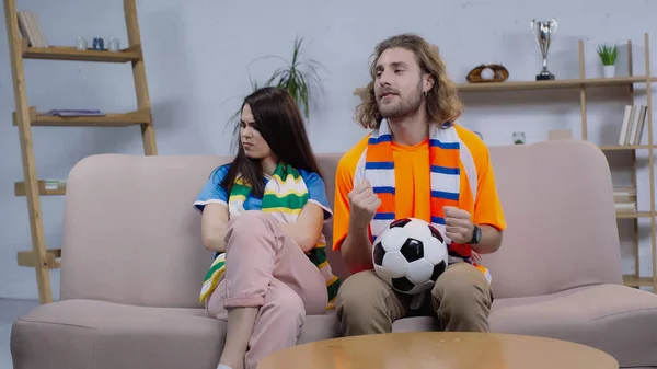 Smiling man holding clenched fists for luck while watching football match near frustrated woman — Fotografia de Stock