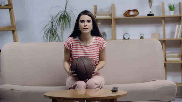 Deporte tenso fan mujer viendo partido de baloncesto en la televisión mientras está sentado en el sofá - foto de stock