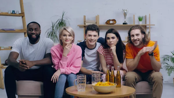 Joyeux amateurs de sport multiethnique regarder la compétition à la télévision près de la bière et des frites sur la table basse — Photo de stock