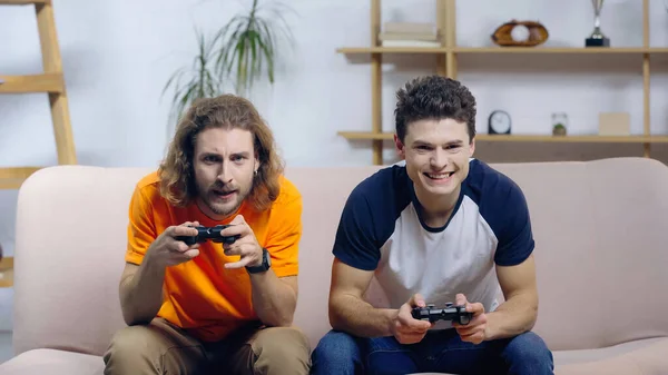 KYIV, UKRAINE - DECEMBER 22, 2021: concentrated and thrilled friends gaming with joysticks at home — Foto stock