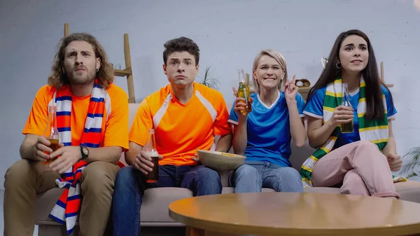 Emocionados fanáticos del deporte con botellas de cerveza viendo la competición deportiva en la televisión en casa - foto de stock