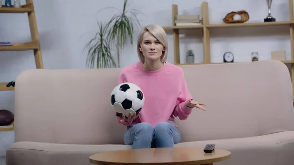 Расстроенная женщина с мячом жестом во время просмотра футбольного чемпионата дома — стоковое фото