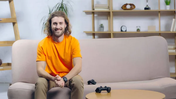 KYIV, UKRAINE - DECEMBER 22, 2021: cheerful man looking at camera while sitting on couch near joysticks — Stockfoto