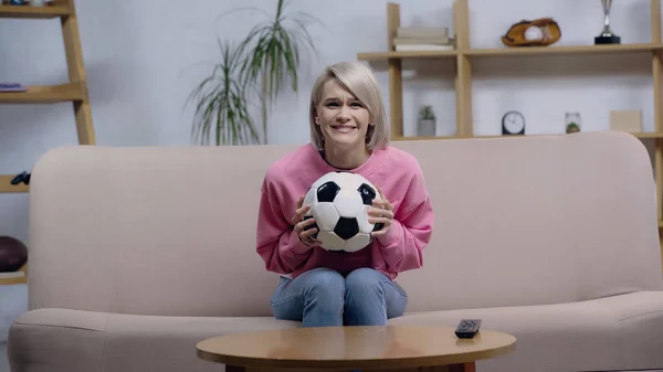 Preocupado deporte fan mujer celebración de pelota de fútbol mientras se ve el juego en la televisión en casa - foto de stock