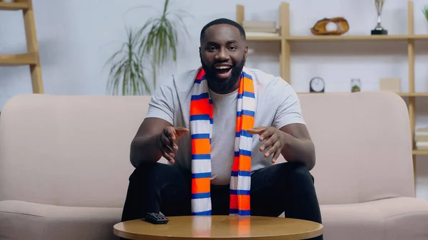 Homme afro-américain joyeux en foulard rayé gestuelle tout en regardant le championnat de sport à la télévision — Photo de stock