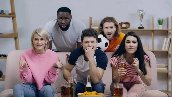 Worried women holding clenched fists for luck while watching football match with multiethnic friends — Stock Photo