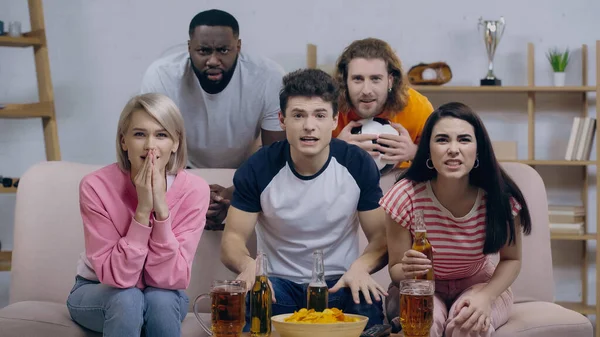 Nervous multiethnic sport fans watching football championship near beer and chips at home — Stock Photo