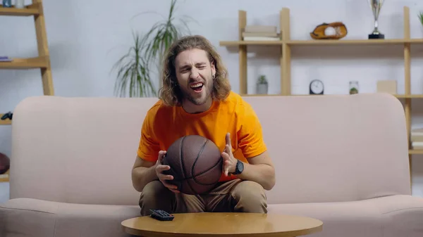 Возбужденный фанат спорта кричать во время просмотра баскетбольного матча на диване дома — стоковое фото