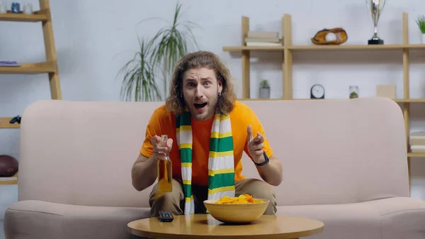 Excited sport fan with bottle of beer holding crossed fingers while watching championship on tv — Fotografia de Stock