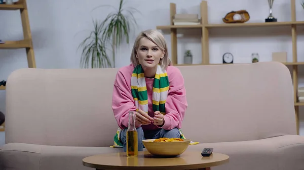 Tense woman in striped scarf watching sport championship near chips and beer on coffee table — Foto stock