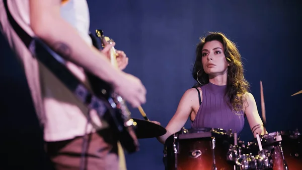 Pretty drummer playing on drums near blurred and tattooed guitarist — Fotografia de Stock